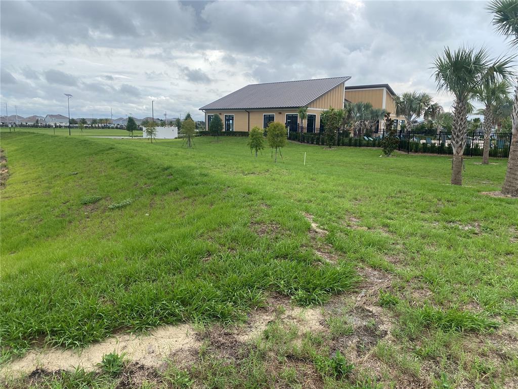 A grassy slope leads toward a community building with a metal roof and palm trees — 2125 LASSO LOOP, EAGLE LAKE, FL