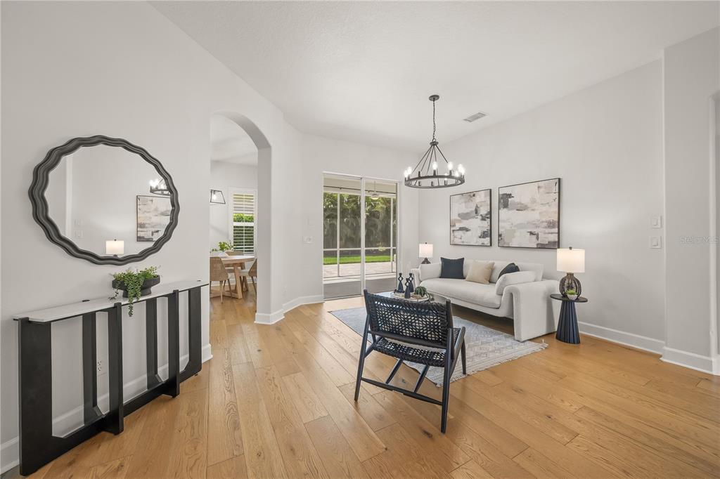 A living room with light wood floors, a white sofa, and a black accent chair — 8275 BARTON FARMS BOULEVARD, SARASOTA, FL