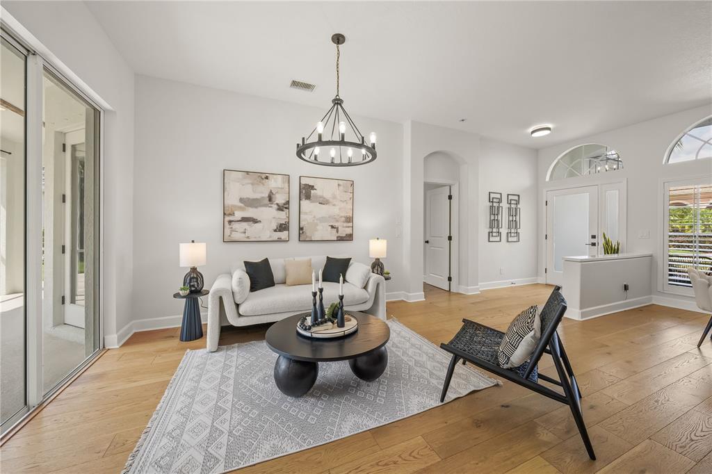 A bright living room features light wood floors, a modern chandelier, and a neutral sofa — 8275 BARTON FARMS BOULEVARD, SARASOTA, FL