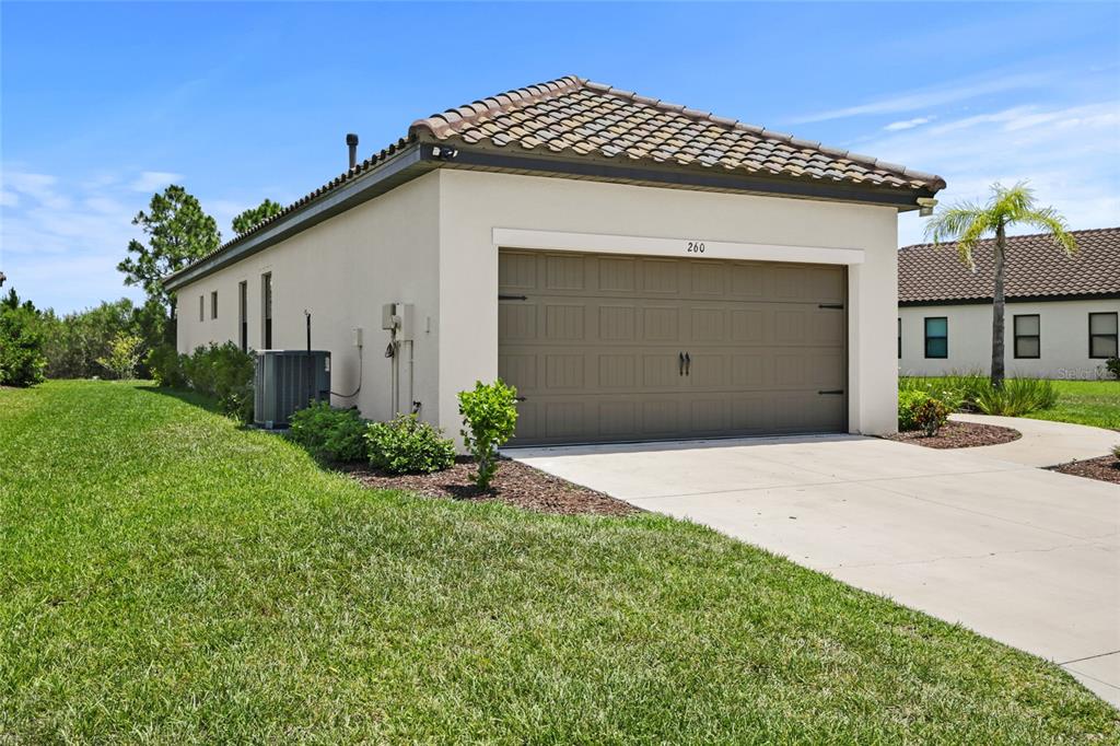 A beige house with a brown garage door and a tiled roof sits on grass — 260 BRIENZA LOOP, NOKOMIS, FL