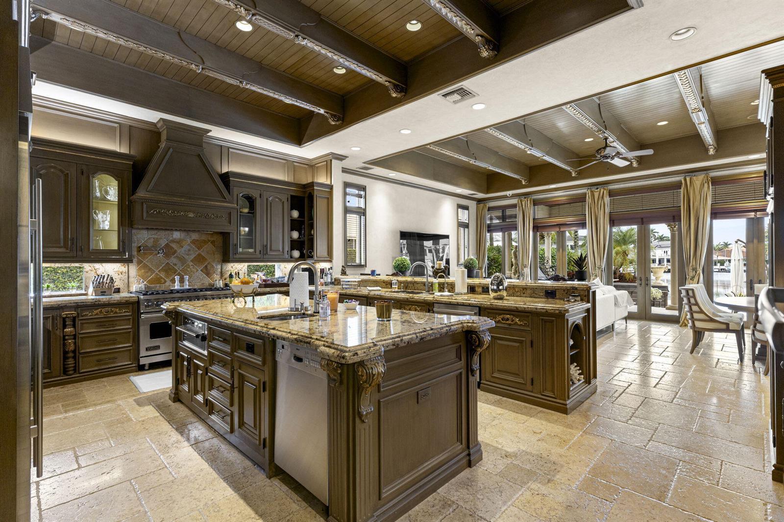 A spacious kitchen features dark wood cabinetry, granite countertops, a large island, and stone flooring — 3131 NE 27th Avenue, Lighthouse Point FL 33064, LIGHTHOUSE POINT, FL