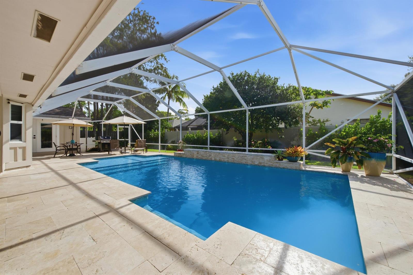 A swimming pool with a stone feature wall sits inside a screened-in patio enclosure — 805 Daffodil Drive, Wellington FL 33414, WELLINGTON, FL