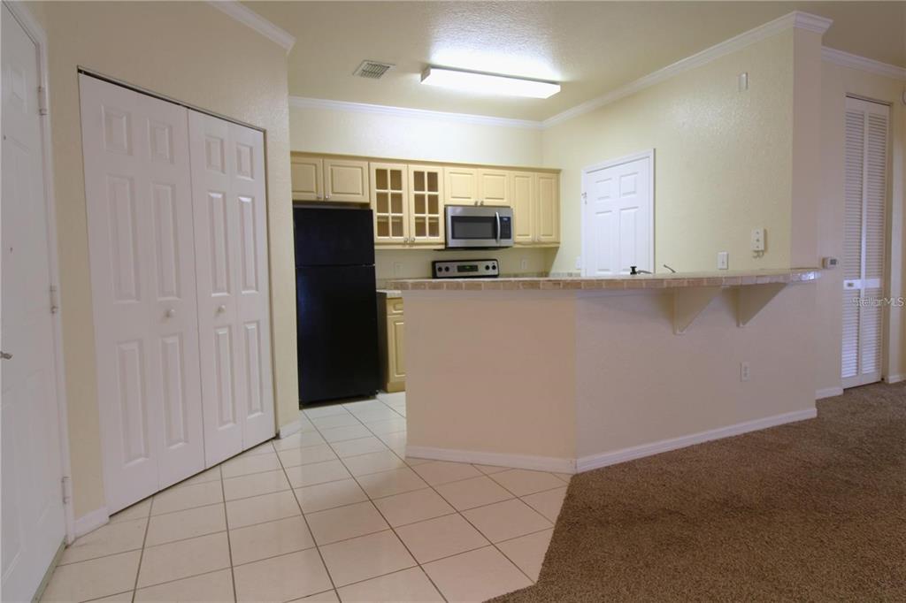 A kitchen features light-colored cabinets, a black refrigerator, a breakfast bar, and tiled flooring — 3561 CONROY ROAD UNIT 217, ORLANDO, FL