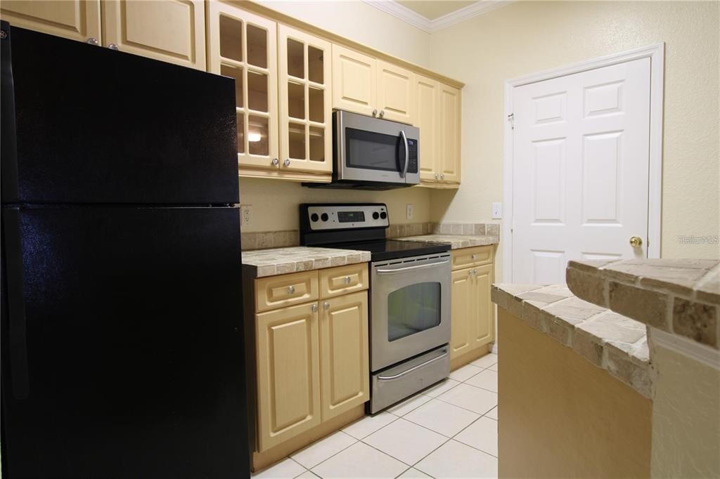 A kitchen features light wood cabinets, tile countertops, and stainless steel appliances — 3561 CONROY ROAD UNIT 217, ORLANDO, FL
