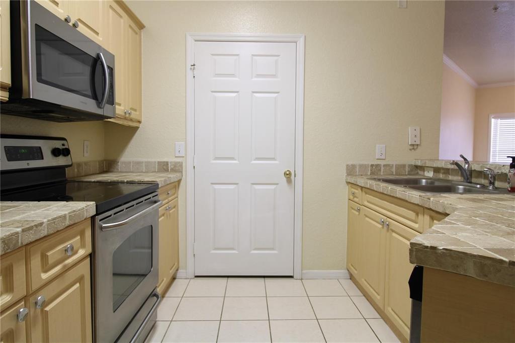 A kitchen features light-colored cabinets, tile countertops, stainless steel appliances, and a white door — 3561 CONROY ROAD UNIT 217, ORLANDO, FL
