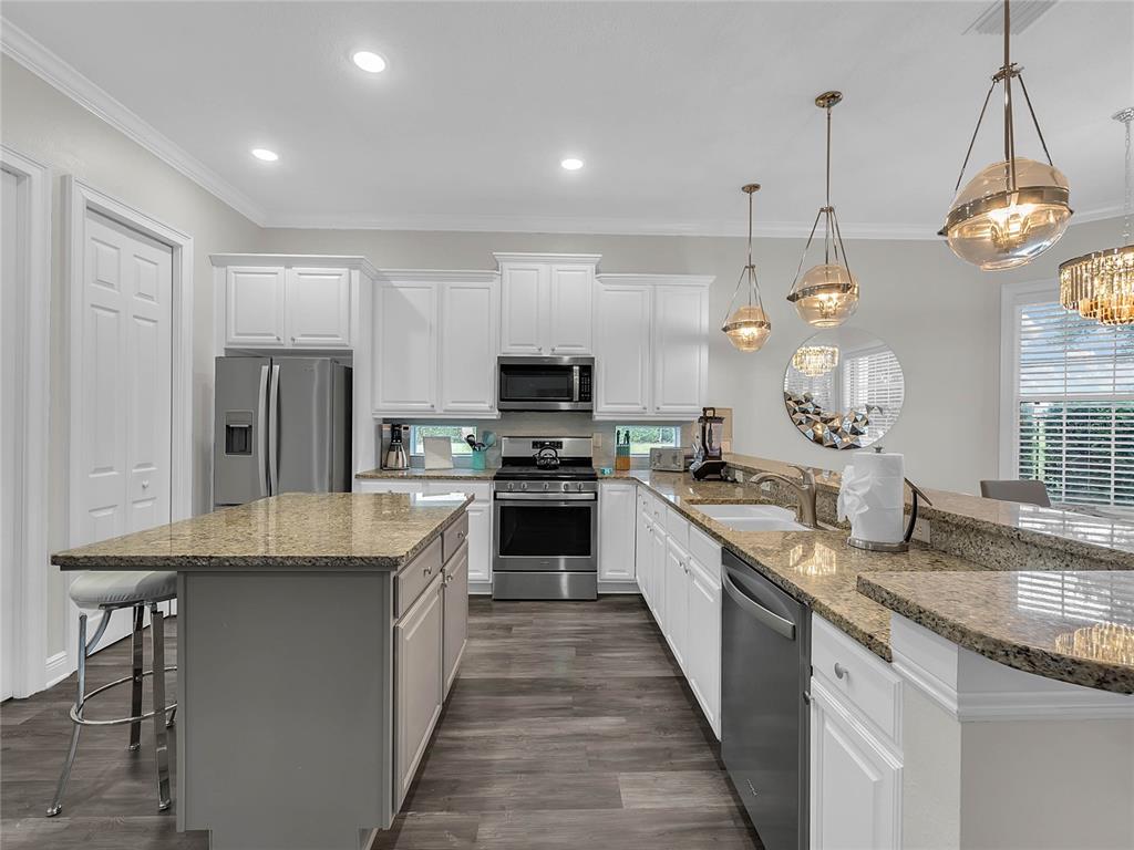 A kitchen with white cabinets, granite countertops, stainless steel appliances, and a gray island — 1231 RADIANT STREET, REUNION, FL
