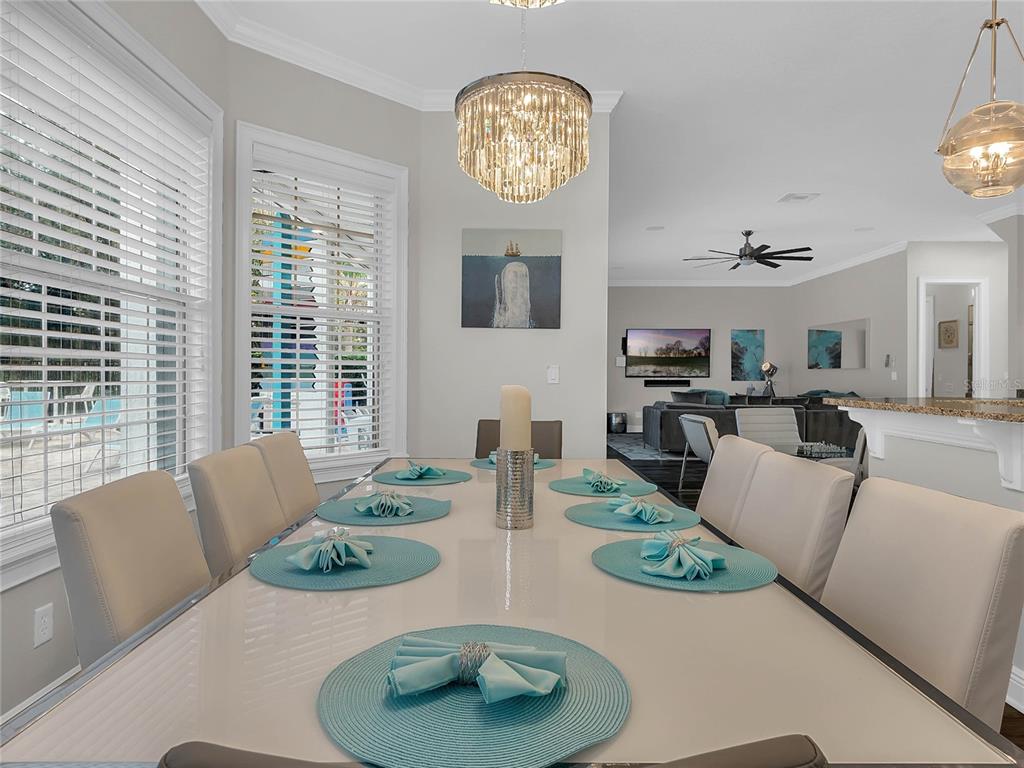 A dining room features a glass table with turquoise placemats, a crystal chandelier, and open-concept living — 1231 RADIANT STREET, REUNION, FL