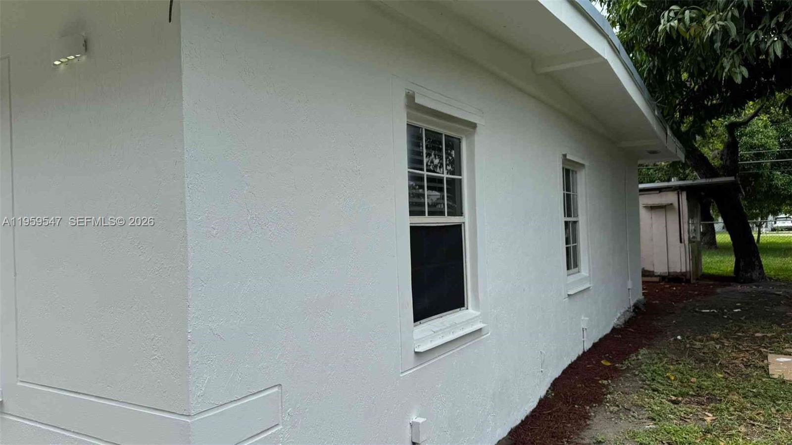 The exterior of a white stucco house features two windows and a small overhang — 16221 E Bunche Park Dr, Miami Gardens FL 33054, MIAMI GARDENS, FL