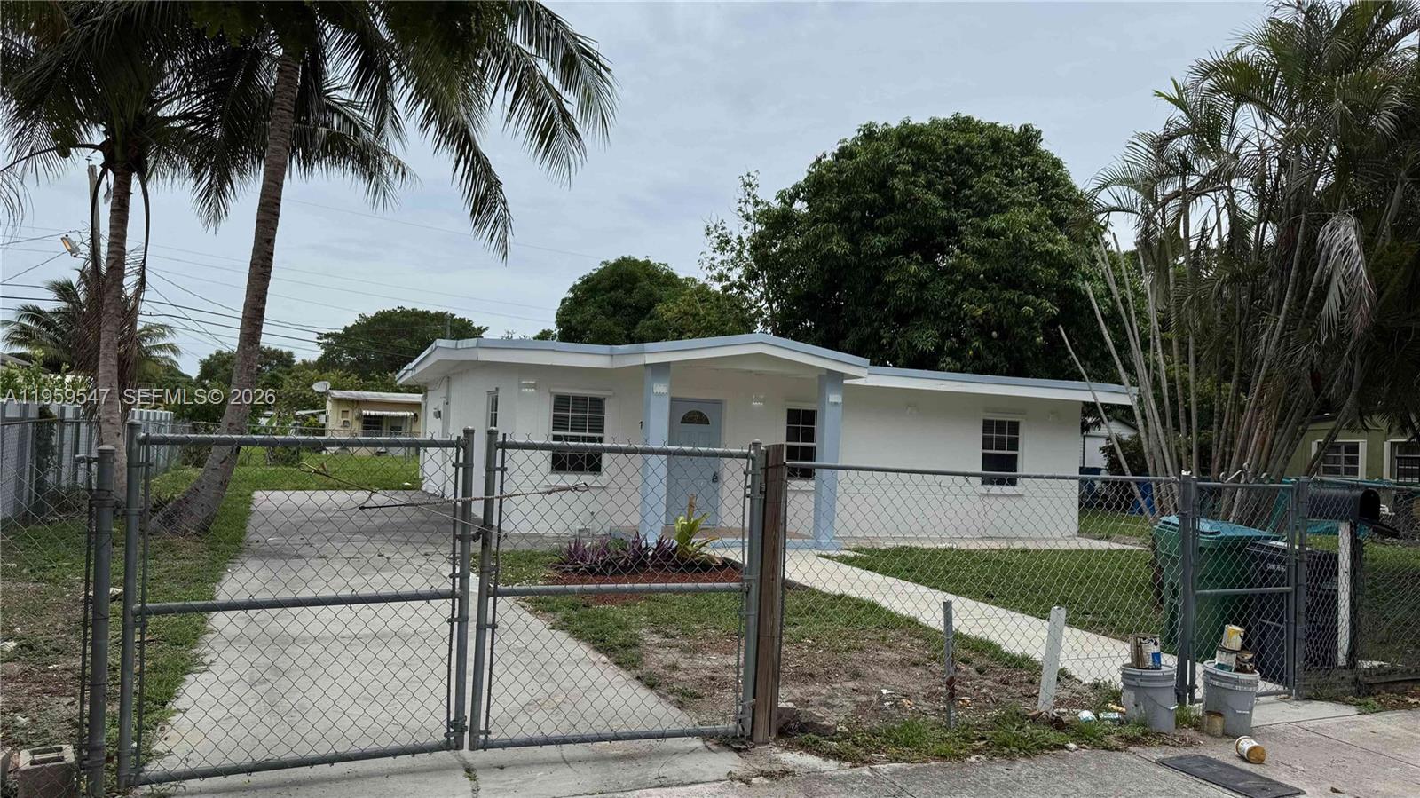 A single-story white house with a chain-link fence and a concrete driveway — 16221 E Bunche Park Dr, Miami Gardens FL 33054, MIAMI GARDENS, FL