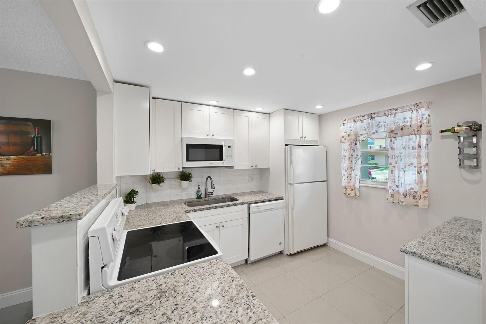 A kitchen features white cabinets, granite countertops, a white stove, and a white refrigerator — 100 Berkley Road # 109, Hollywood FL 33024, HOLLYWOOD, FL