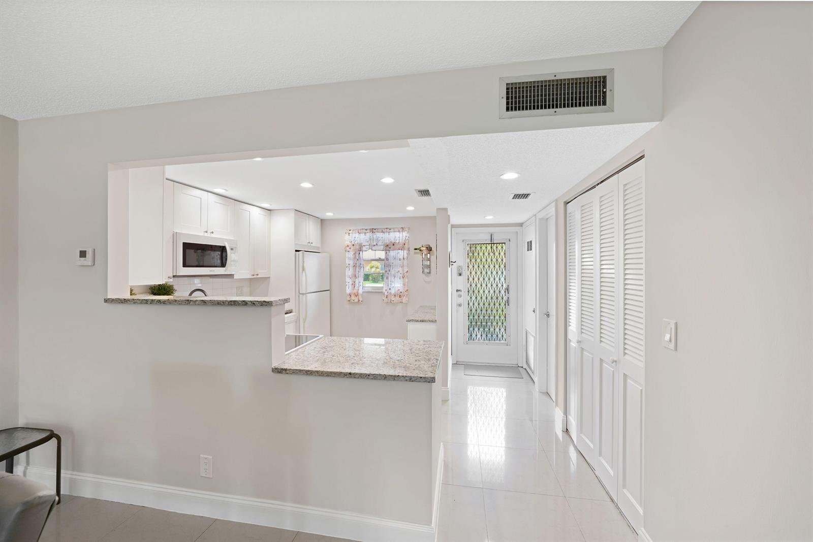 A kitchen with white cabinets, granite countertops, and tile flooring opens to an entryway — 100 Berkley Road # 109, Hollywood FL 33024, HOLLYWOOD, FL
