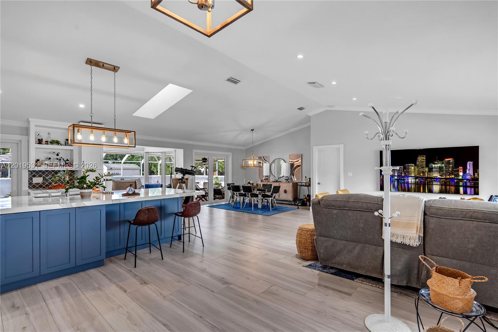 This open-concept living room and kitchen features light wood flooring, a blue island, and vaulted ceilings — 1501 NW 20th St, Homestead FL 33030, HOMESTEAD, FL