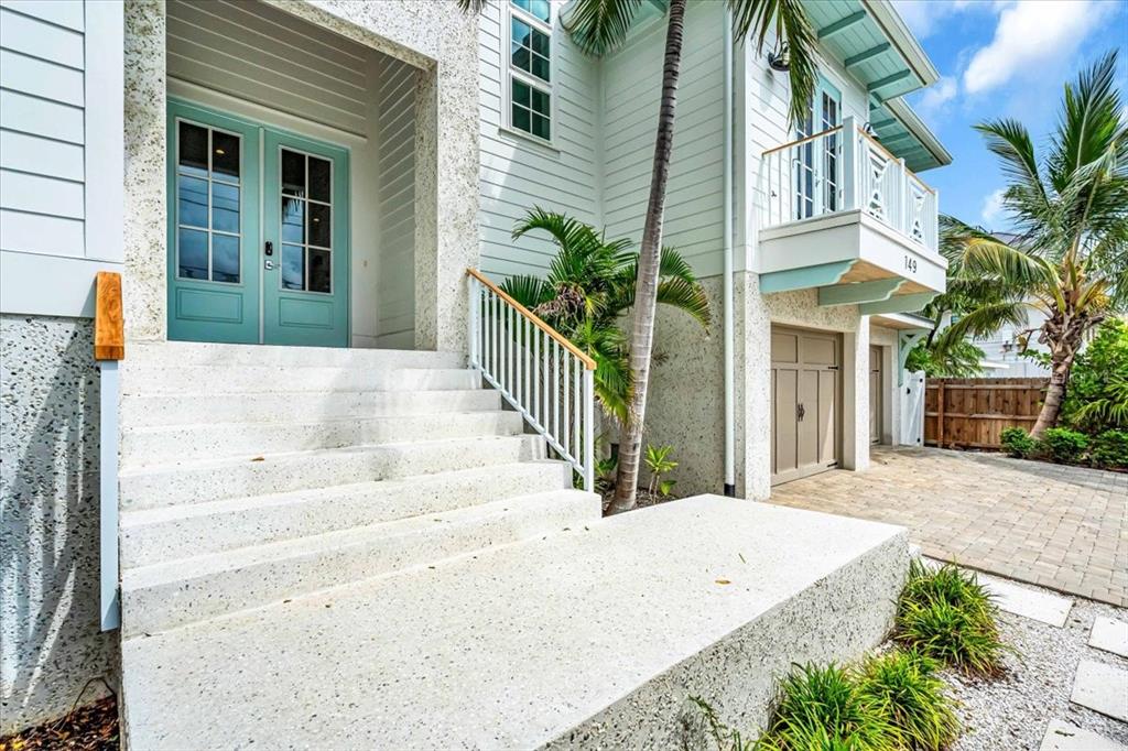 The exterior of a coastal home features light-colored siding, a turquoise front door, and stairs — 149 MCKINLEY DRIVE, SARASOTA, FL