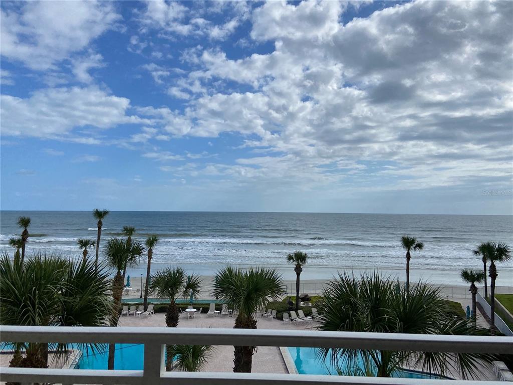 A view from a balcony overlooking a swimming pool, palm trees, beach, and ocean — 2401 S ATLANTIC AVENUE UNIT E204, NEW SMYRNA BEACH, FL