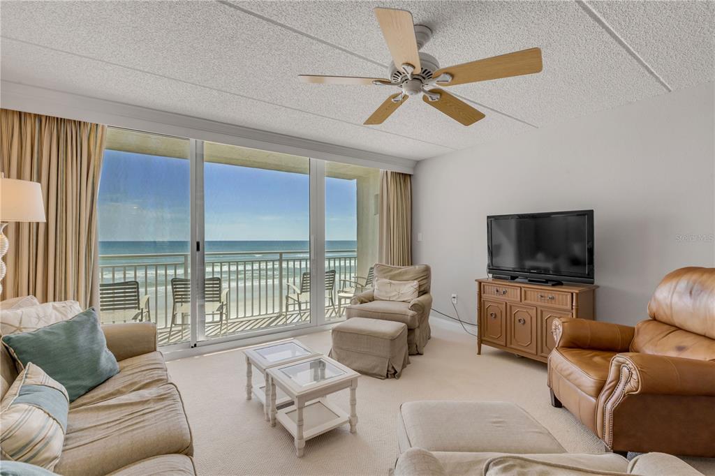 A living room features a ceiling fan, a television, and a balcony overlooking the ocean — 2401 S ATLANTIC AVENUE UNIT E204, NEW SMYRNA BEACH, FL