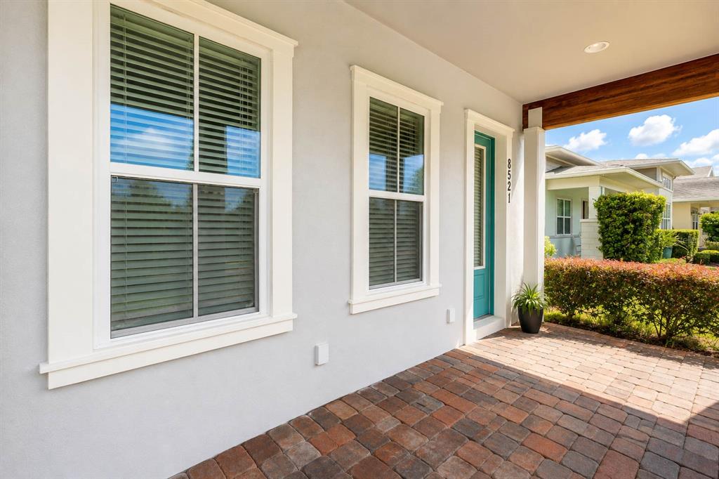 A covered brick porch features a teal front door, two windows, and a wooden beam — 8521 DUBOCHET STREET, ORLANDO, FL