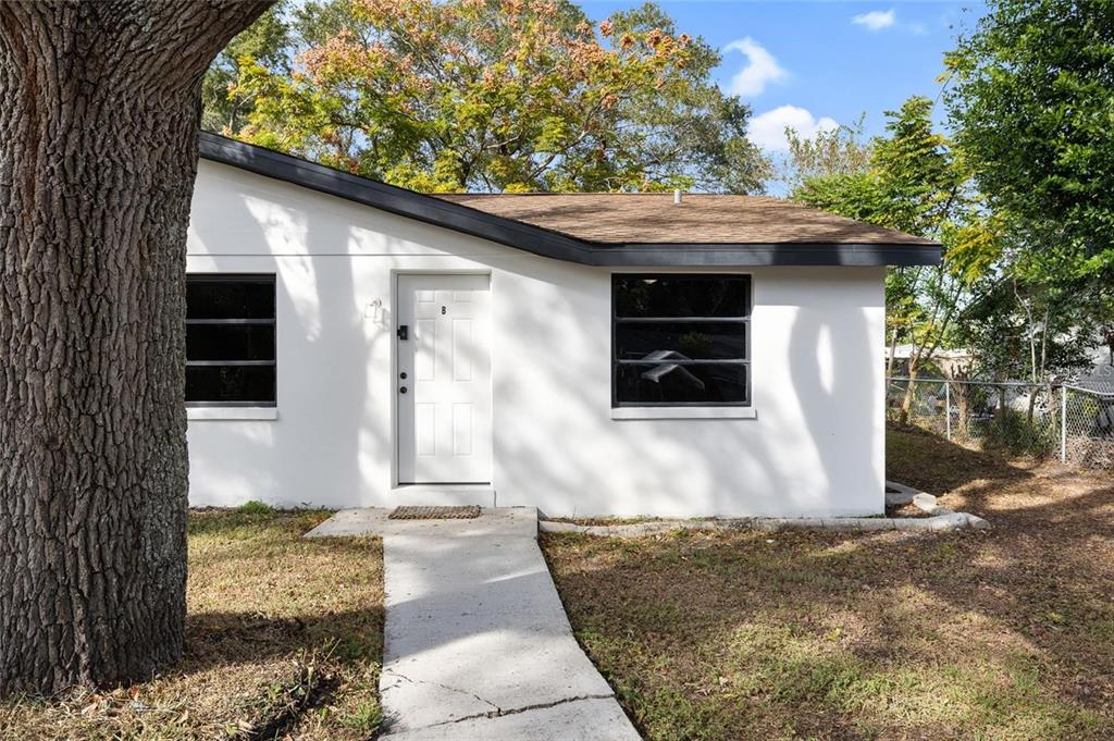 A white single-story house exterior features a front door, two windows, and a concrete walkway — 1220 E 142ND AVENUE UNIT B, TAMPA, FL