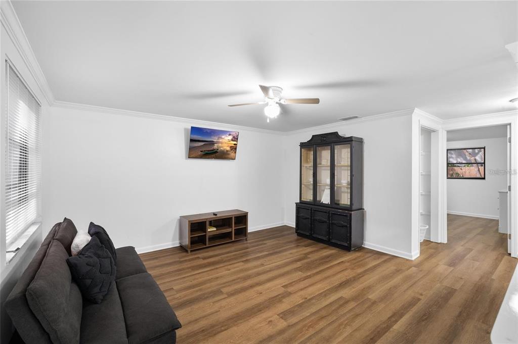 A living room with wood-look flooring, a dark sofa, a television, and a black hutch — 1220 E 142ND AVENUE UNIT B, TAMPA, FL