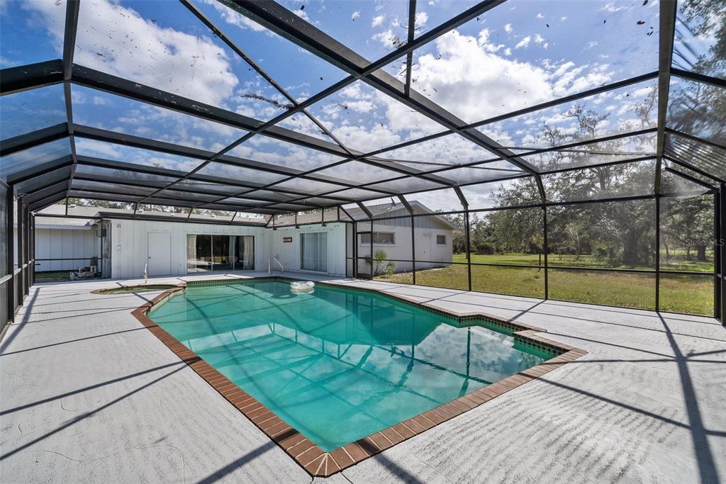 A screened-in swimming pool with a concrete deck sits behind a white house — 1510 LENA LANE, SARASOTA, FL