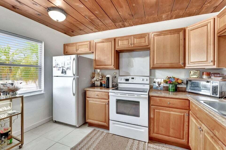 A kitchen features light wood cabinets, white appliances, tile flooring, and a wood-paneled ceiling — 329 SE 3rd Avenue, Delray Beach FL 33483, DELRAY BEACH, FL