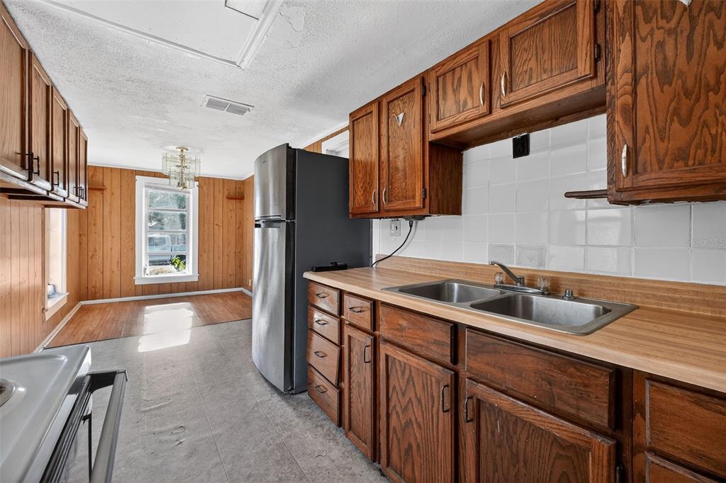 A kitchen features wood cabinets, a laminate countertop, a stainless steel refrigerator, and wood paneling — 146 KINGSTON AVENUE, DAYTONA BEACH, FL