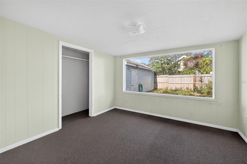 A bedroom with pale green paneled walls, dark carpet, a closet, and a large window — 146 KINGSTON AVENUE, DAYTONA BEACH, FL