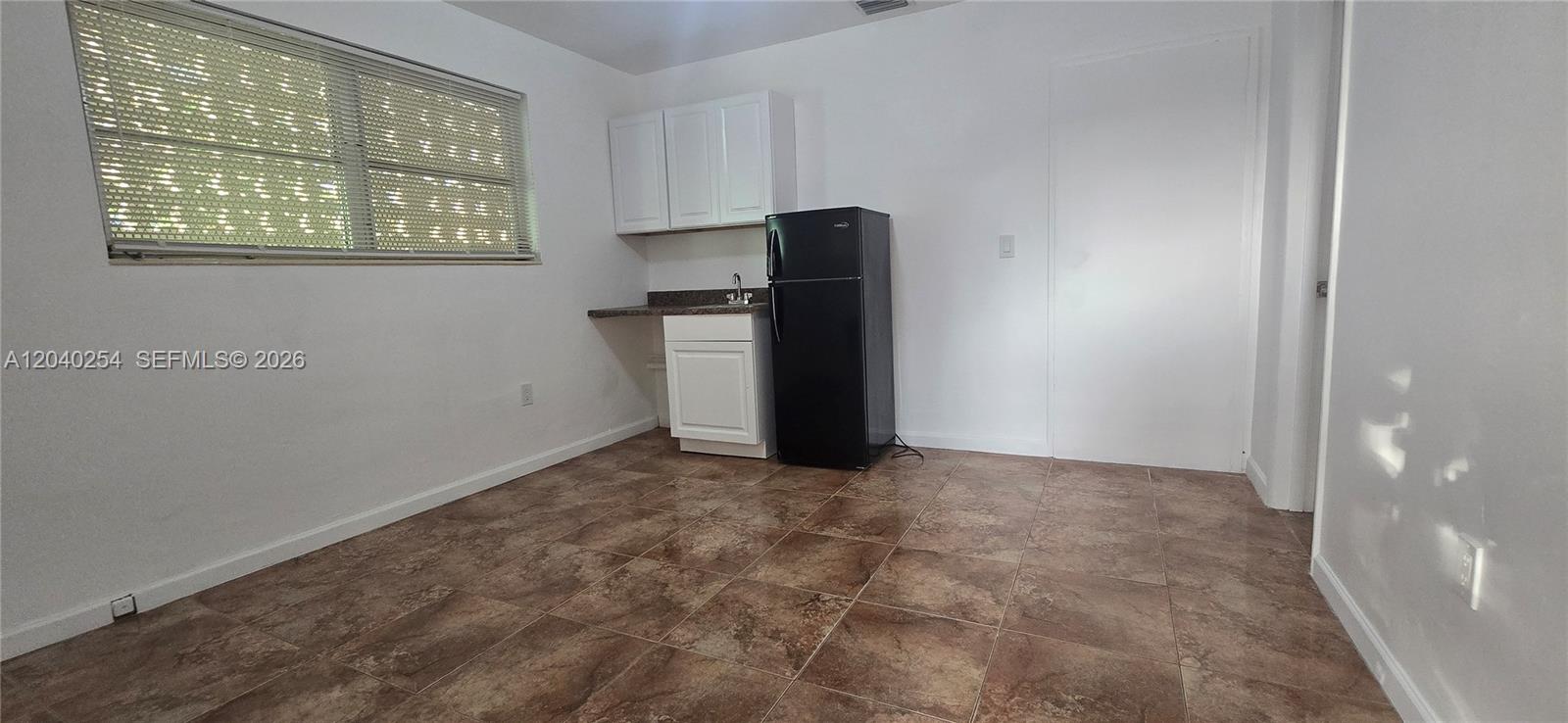 This kitchen features white cabinets, a black refrigerator, and brown tile flooring — 201 SW 30th Ct, Miami FL 33135, MIAMI, FL