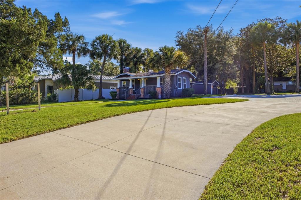 A single-story house with a dark exterior and a large concrete driveway sits among trees — 527 NE 8TH AVENUE, OCALA, FL