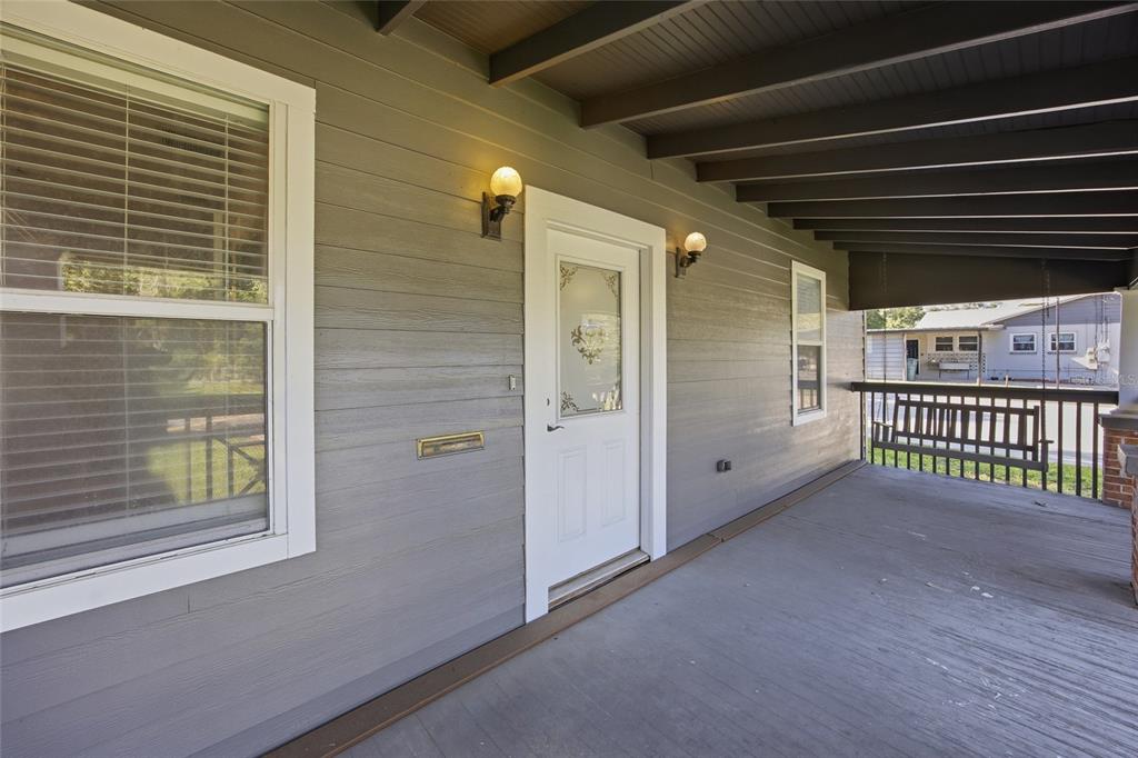 A covered porch with gray siding, a white front door, and a wooden porch swing — 527 NE 8TH AVENUE, OCALA, FL