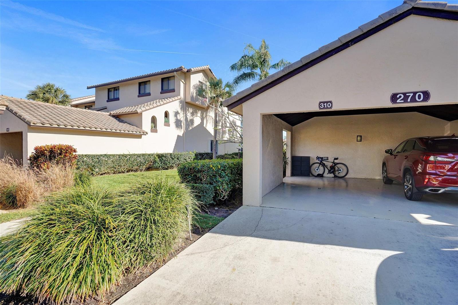 A beige stucco building features a covered carport with a bicycle and a parked car — 270 Captains Walk # 310, Delray Beach FL 33483, DELRAY BEACH, FL
