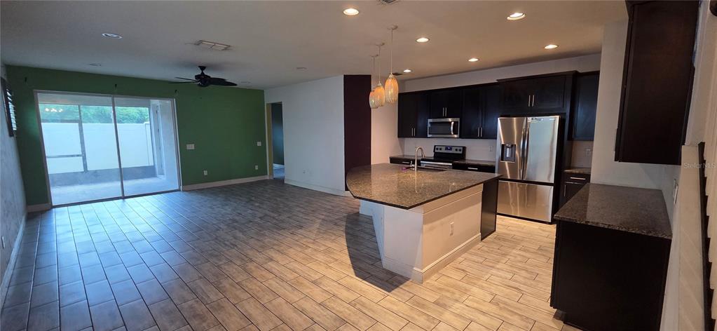 A kitchen with dark cabinets and a granite island opens to a living area — 10322 HOLSTEIN EDGE PLACE, RIVERVIEW, FL