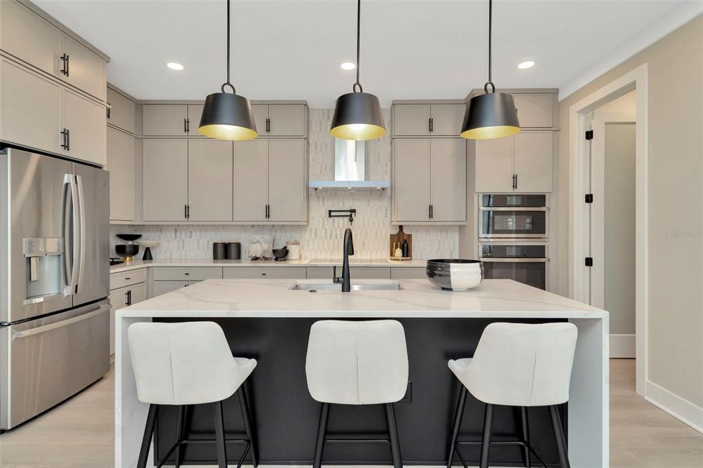 A modern kitchen features a white quartz island, gray cabinetry, and three black pendant lights — 3904 ROCKY ISLAND ROAD, NEW PORT RICHEY, FL