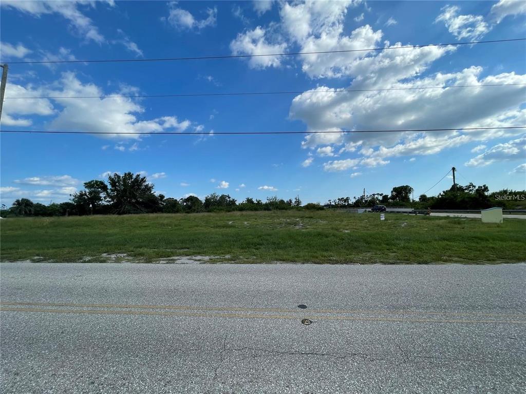 A vacant, grassy lot sits alongside a paved road under a blue, cloudy sky — 12743 FORESMAN BLVD, PORT CHARLOTTE, FL