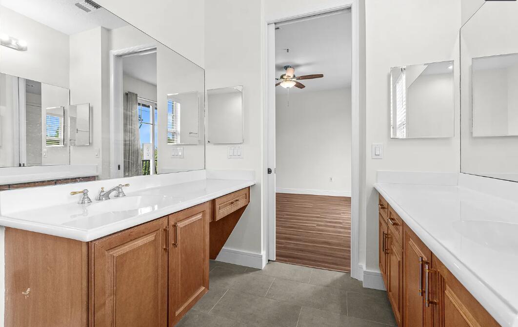 A bathroom with dual wooden vanities, white countertops, large mirrors, and gray tile flooring — 536 N West 39th Circle, Boca Raton FL 33431, BOCA RATON, FL