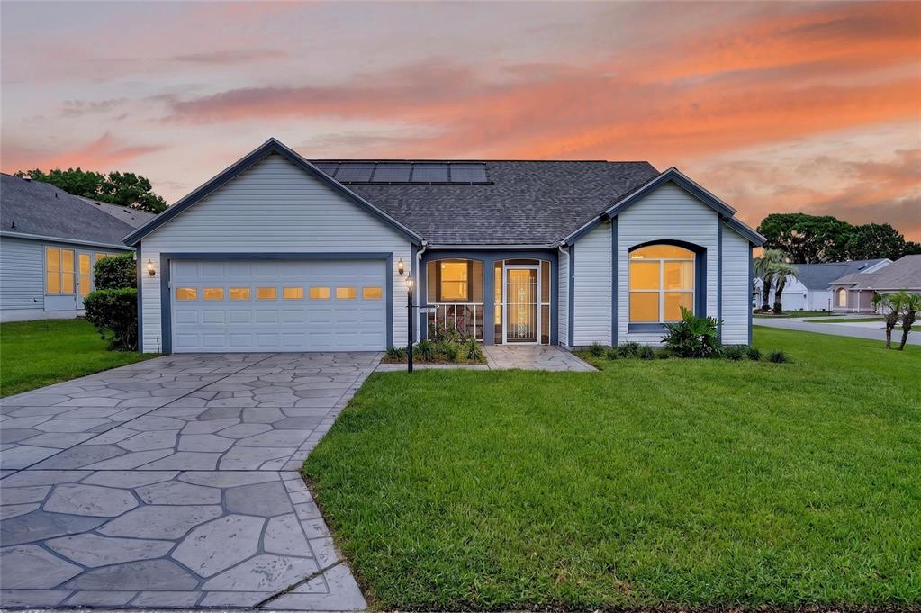 A single-story house with light siding, a stone-patterned driveway, and solar panels on the roof — 1101 MONTEREY LANE, THE VILLAGES, FL
