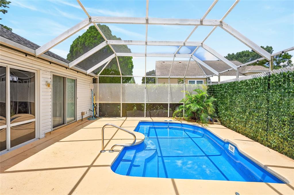 A screened-in patio features a rectangular swimming pool with a metal handrail and privacy lattice — 1101 MONTEREY LANE, THE VILLAGES, FL