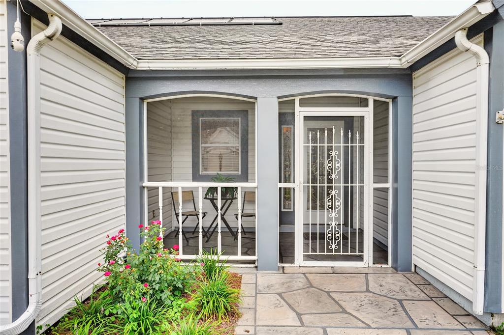 A front entryway features a screened porch, a white security door, and stone-patterned concrete flooring — 1101 MONTEREY LANE, THE VILLAGES, FL