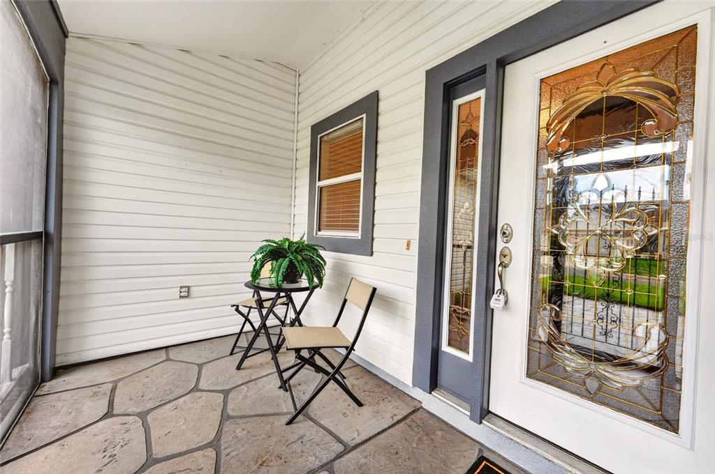 A covered porch features stone flooring, white siding, a small bistro set, and a decorative door — 1101 MONTEREY LANE, THE VILLAGES, FL