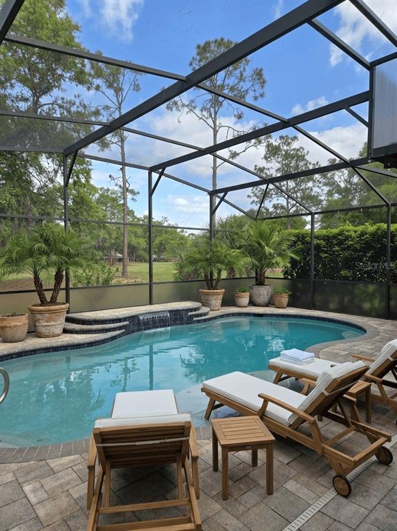 A screened-in swimming pool with lounge chairs on a paver patio and potted palm trees — 5084 GREENS DRIVE, LADY LAKE, FL