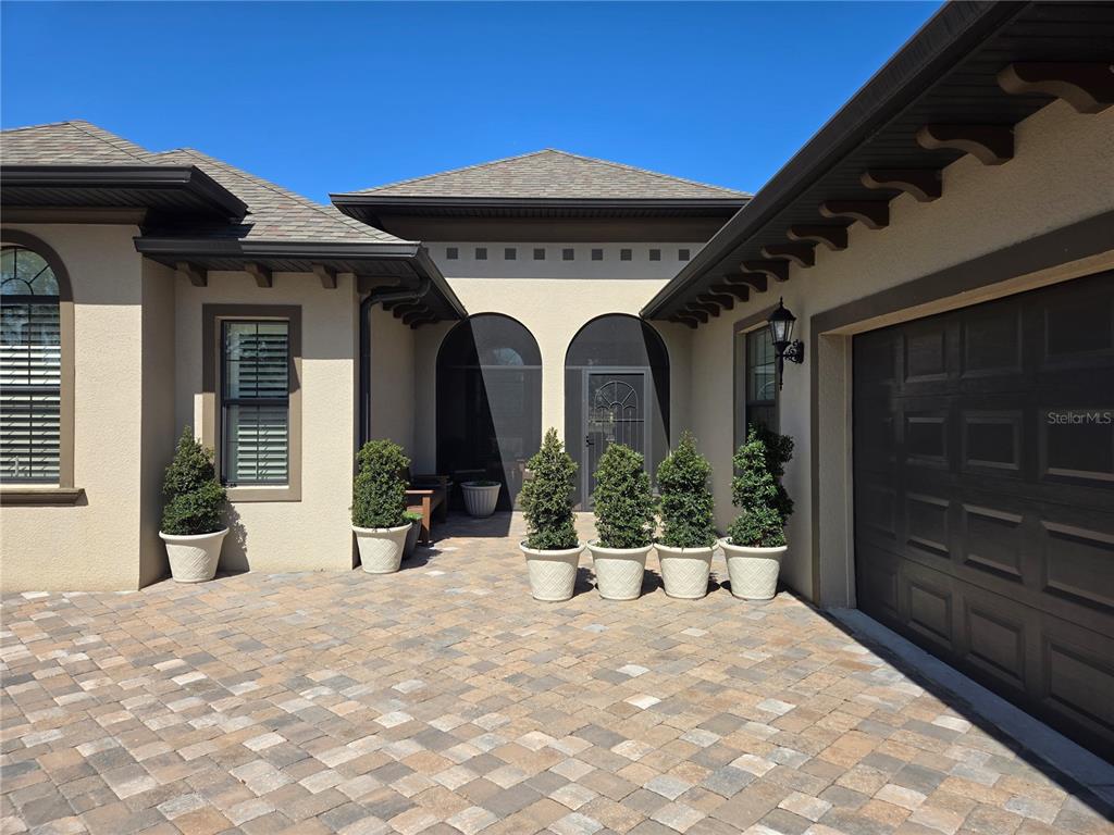 The exterior of a house features a paver driveway, potted topiaries, and a screened entryway — 5084 GREENS DRIVE, LADY LAKE, FL