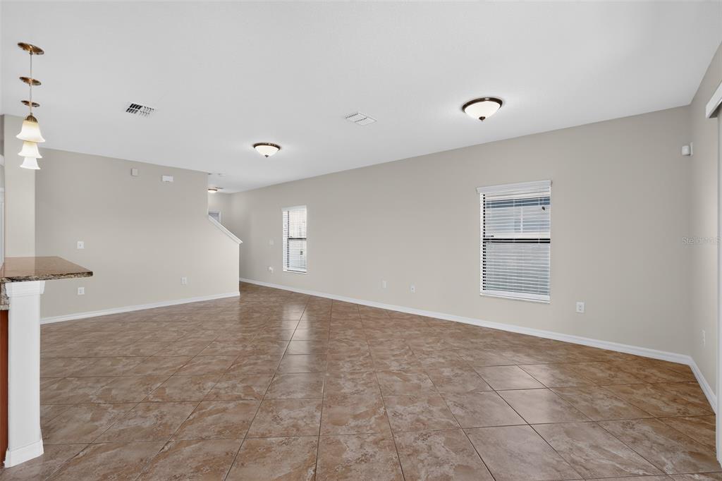 An open-concept living area features beige walls, tile flooring, and two windows with blinds — 10105 NEWMINSTER LOOP, SUN CITY CENTER, FL
