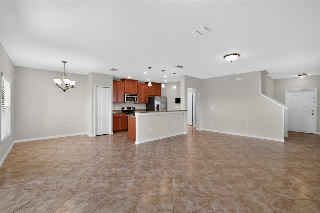 An open-concept kitchen with wood cabinets and tile flooring overlooks a spacious living area — 10105 NEWMINSTER LOOP, SUN CITY CENTER, FL