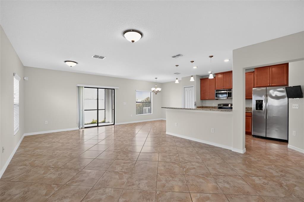 An open-concept living area features tile flooring, a kitchen with wood cabinets, and sliding doors — 10105 NEWMINSTER LOOP, SUN CITY CENTER, FL