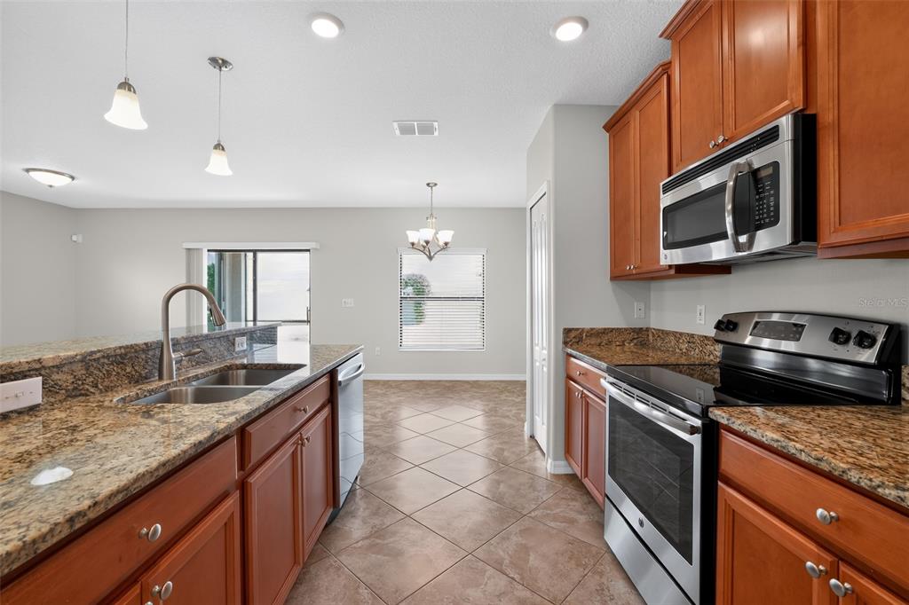 A kitchen with wood cabinets, granite countertops, and stainless steel appliances overlooks a dining area — 10105 NEWMINSTER LOOP, SUN CITY CENTER, FL