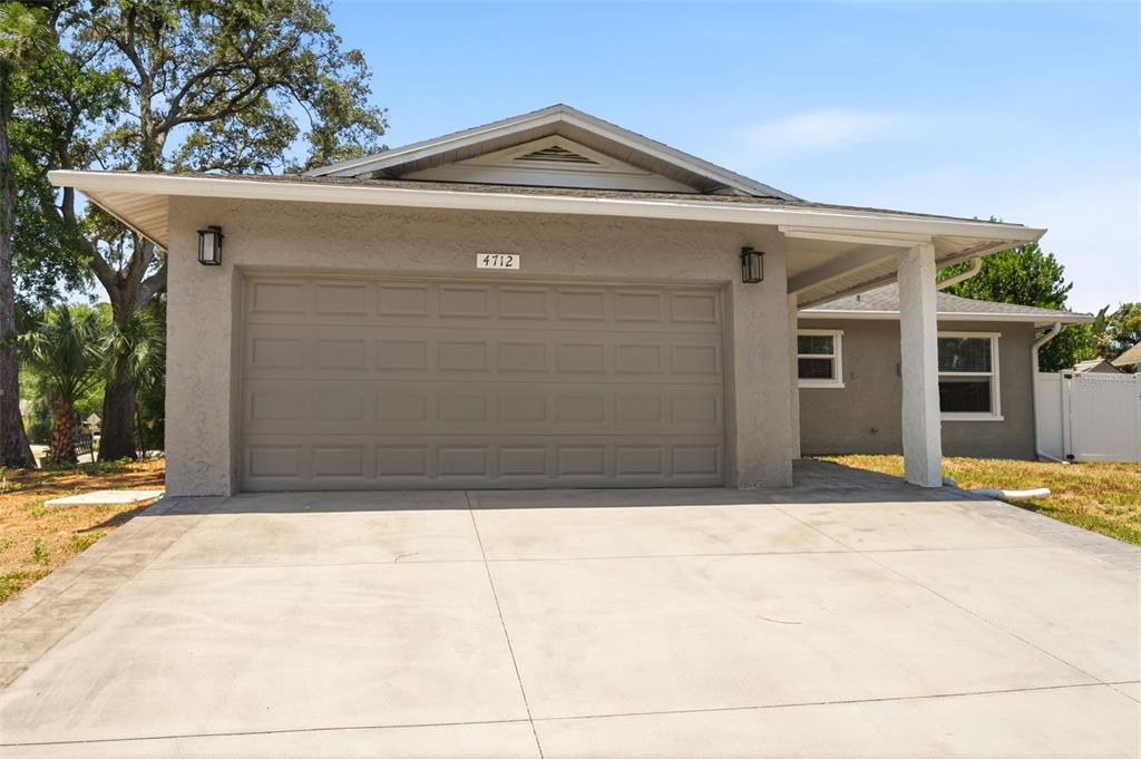 A single-story house exterior features a beige stucco finish, a two-car garage, and a driveway — 4712 SIMCOE STREET, PALM HARBOR, FL