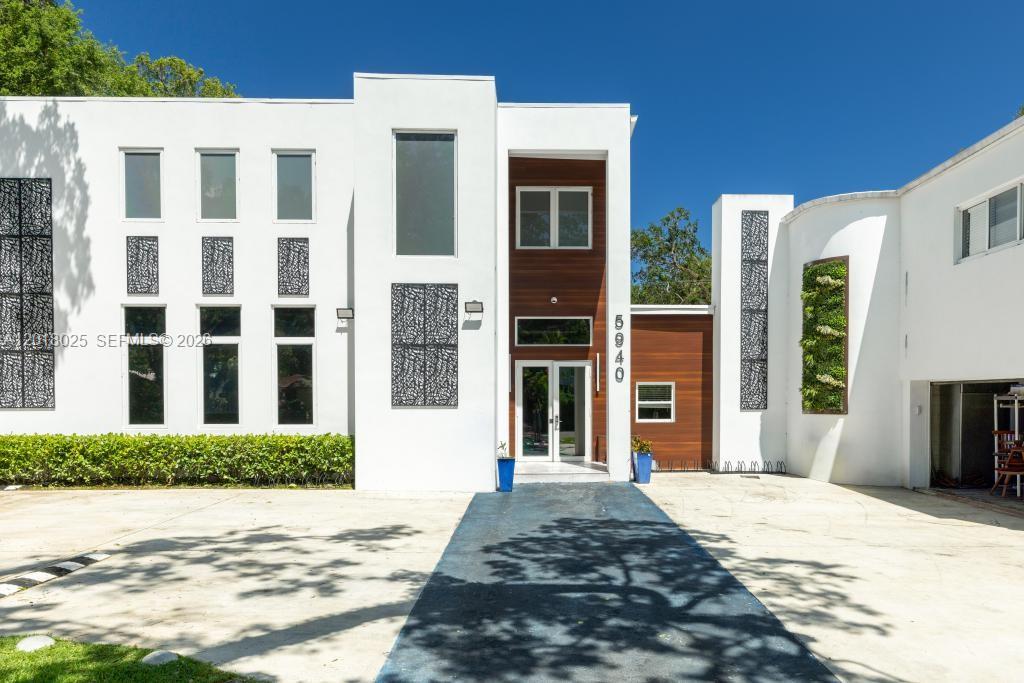The exterior of a modern white house features wood paneling, decorative metal screens, and landscaping — 5940 SW 37th Ave, Dania Beach FL 33312, DANIA BEACH, FL