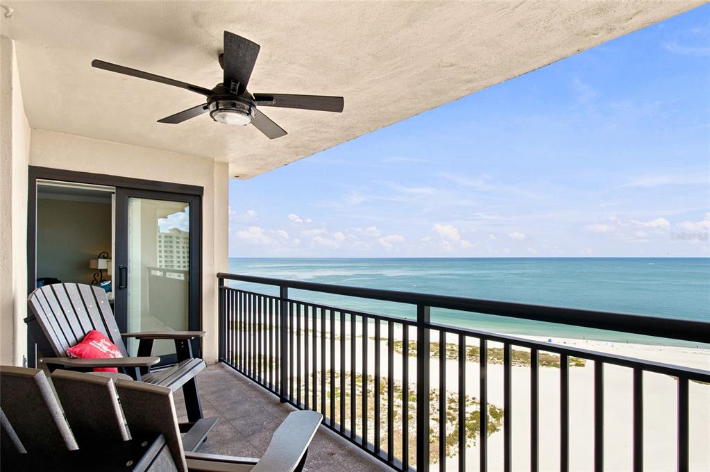 A balcony with dark chairs and a ceiling fan overlooks a sandy beach and ocean — 1270 GULF BOULEVARD UNIT 2007, CLEARWATER BEACH, FL