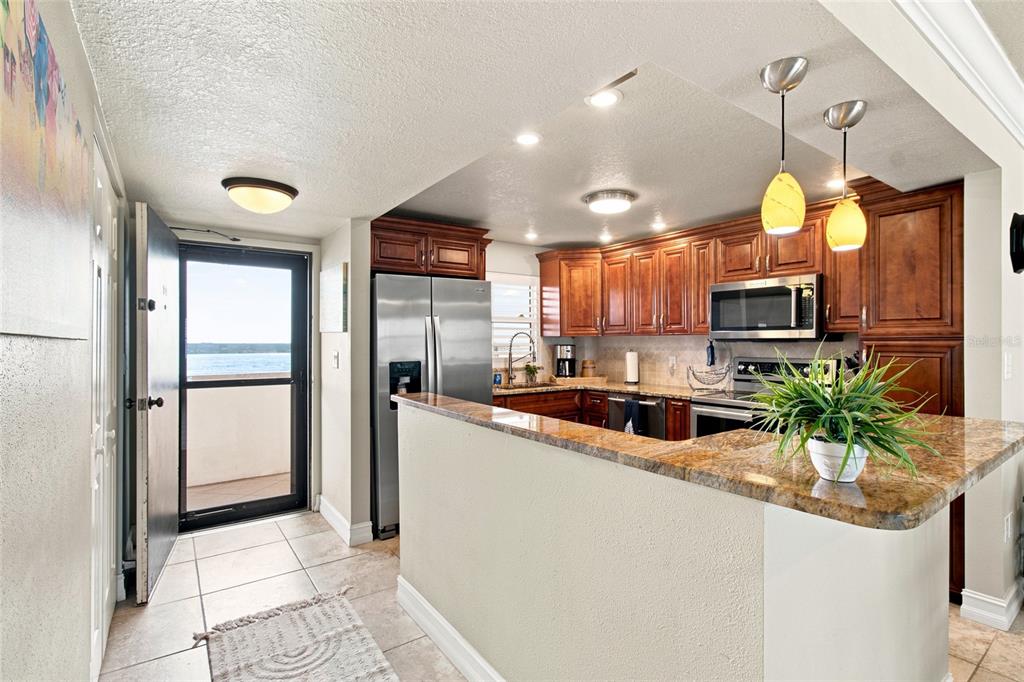 A kitchen with wood cabinets, granite countertops, and a door opening to a water view — 1270 GULF BOULEVARD UNIT 2007, CLEARWATER BEACH, FL