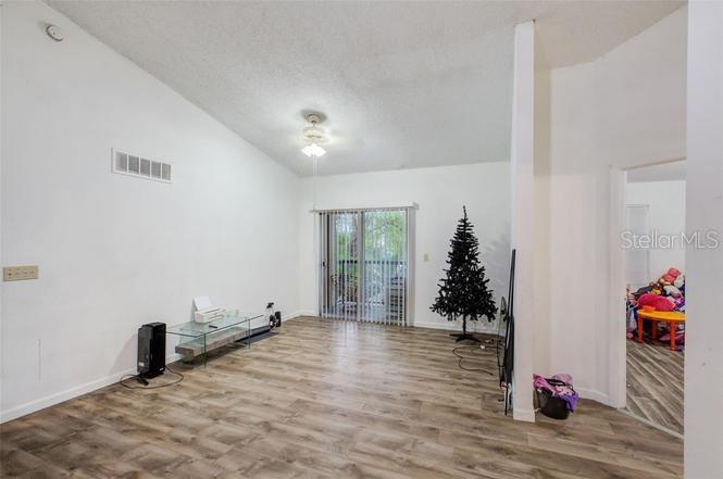 A living room with wood-look flooring, a glass console table, and a sliding glass door — 1956 LAKE ATRIUMS CIRCLE UNIT 141, ORLANDO, FL