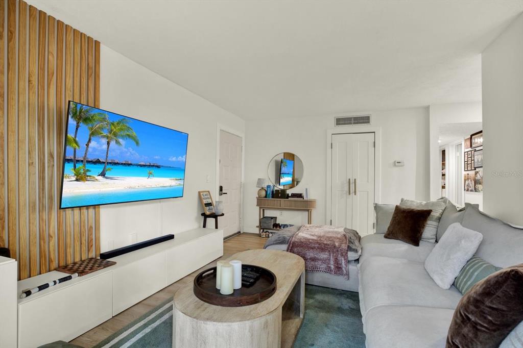 A living room features a wall-mounted television, wood slat accent wall, and a light-colored sofa — 10800 US HIGHWAY 19 N UNIT 136, PINELLAS PARK, FL